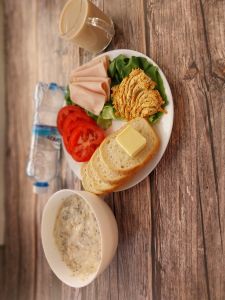 Zdjęcie przedstawia Dietę łatwostrawną: Kawa zbożowa z mlekiem Owsianka budyniowa z bananem i jabłkiem z posypką chia Bułka pszenna długa krojona Masło extra Szynka Drobiowa, parzona, z dodatkiem białka wieprzowego Pomidor Woda mineralna Sałata lodowa Pasta z tofu i pieczonej marchewki